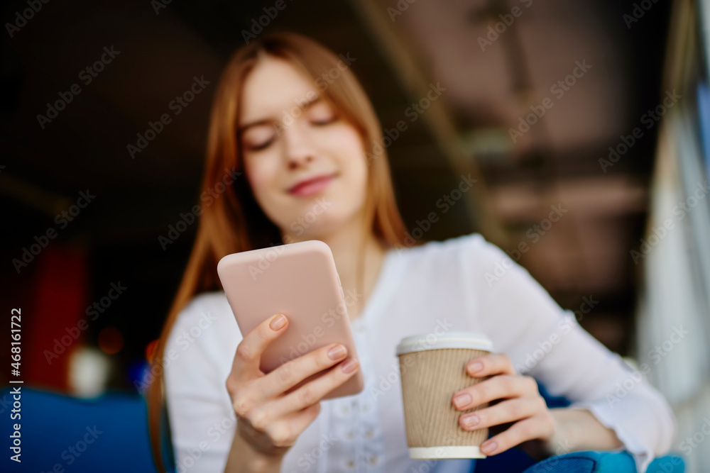 Blurred female blogger with coffee to go using cellphone gadget for browsing internet website during leisure, millennial woman checking mobility notification for installing communication app Blurred female blogger with coffee to go using cellphone gadget for browsing internet website during leisure, millennial woman checking mobility notification for installing communication app