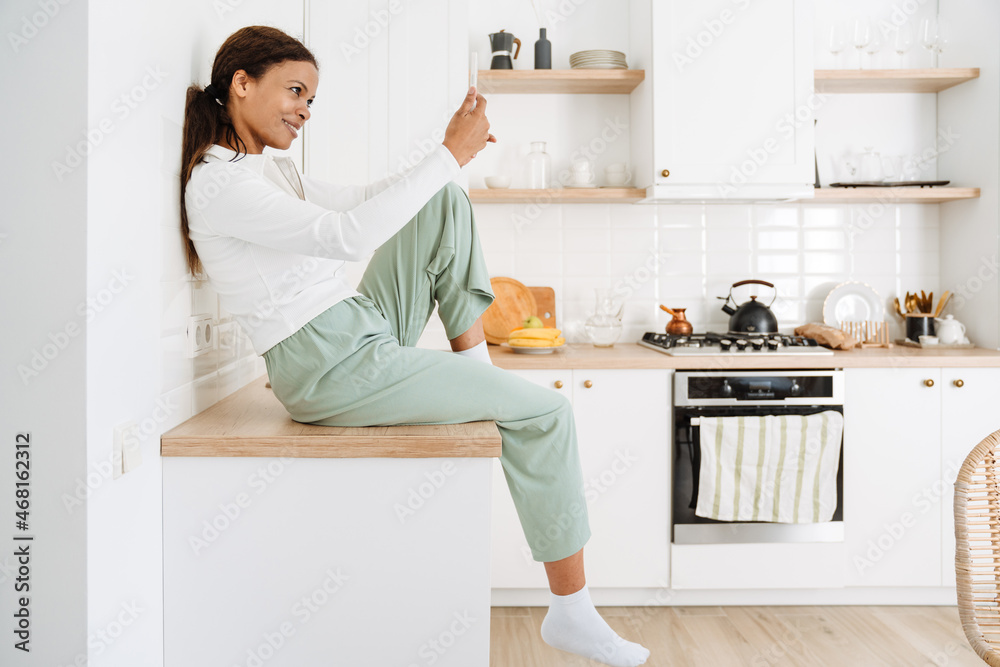 Young black woman smiling while using cellphone in kitchen Young black woman smiling while using cellphone in kitchen