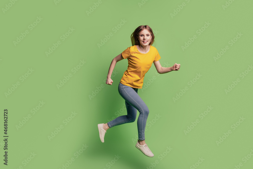 Portrait of charming cheerful lady jump run hurry wear yellow t-shirt jeans sneakers on green background