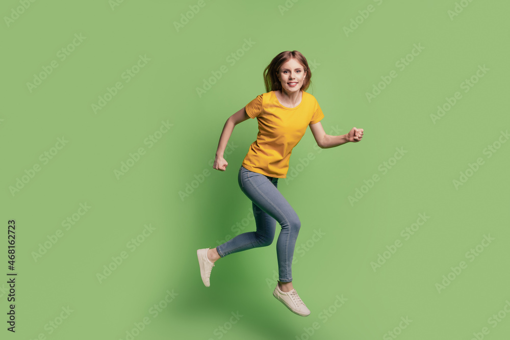 Portrait of charming cheerful lady jump run hurry wear yellow t-shirt jeans sneakers on green background Portrait of charming cheerful lady jump run hurry wear yellow t-shirt jeans sneakers on green background
