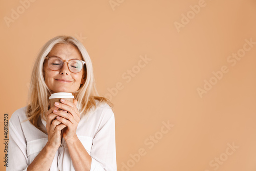 Mature woman in eyeglasses smiling while drinking coffee
