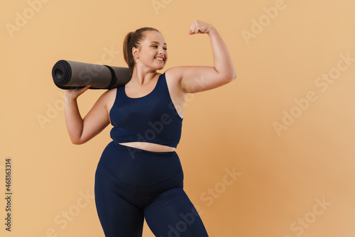 Fototapeta Naklejka Na Ścianę i Meble -  Young woman showing her bicep while posing with fitness mat