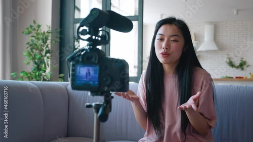 Happy young asian woman blogger filming new vlog video with professional camera mounted on tripod in kitchen at home. Blogging concept. photo