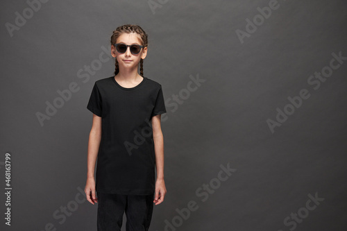 Kid girl wearing black t-shirt with space for your logo or design in studio over gray background with sunglasses