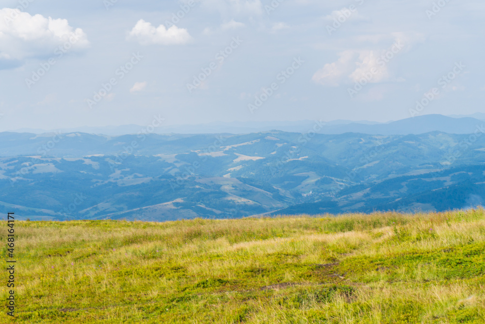 Scenic panoramic view of idyllic rolling hills landscape with blooming meadows mountain peaks in the background on a beautiful sunny day with blue sky and clouds in springtime