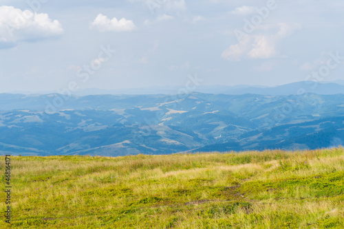 Scenic panoramic view of idyllic rolling hills landscape with blooming meadows mountain peaks in the background on a beautiful sunny day with blue sky and clouds in springtime © Ivanna