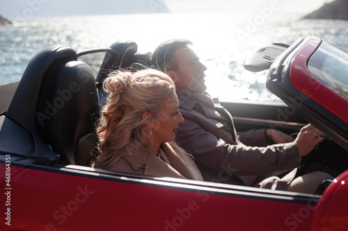 Happy couple, woman and man hugging outdoor and trevelling in the convertible red car. People dressed fashion coat photo