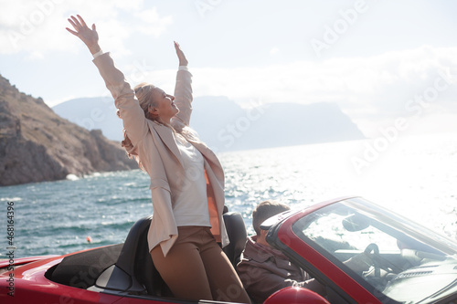 Happy couple, woman and man hugging outdoor and trevelling in the convertible red car. People dressed fashion coat photo