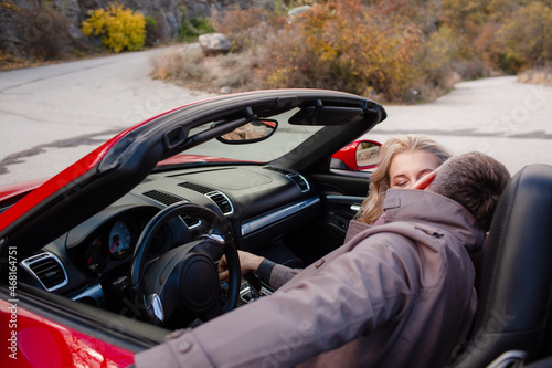 Happy couple, woman and man hugging outdoor and trevelling in the convertible red car. People dressed fashion coat photo