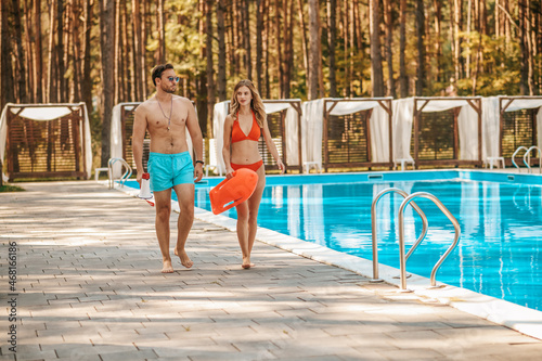 Two pool lifeguards walking near the public pool and talking photo