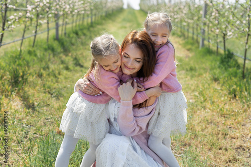 Portrait of a mother and her twin daughters in a blooming Apple orchard. Girls hug their mother