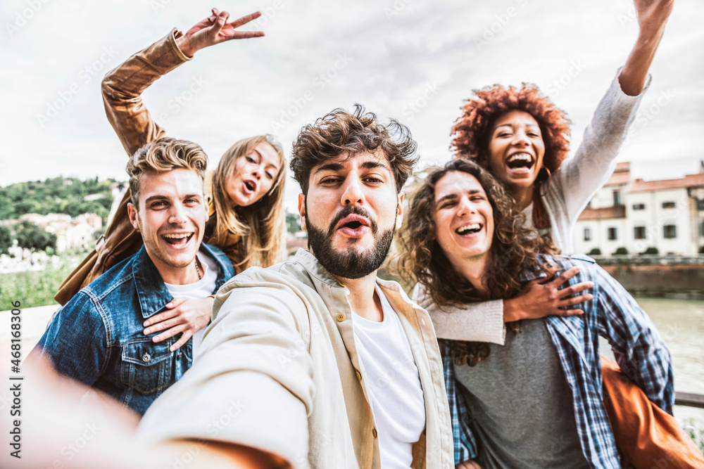 Fototapeta premium Multicultural happy friends having fun taking group selfie portrait on city street - Young diverse people celebrating laughing together outdoors - Happy lifestyle concept.