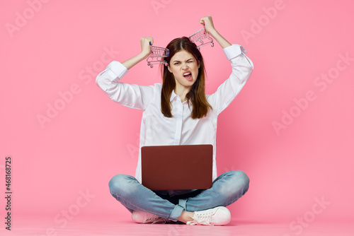 woman sitting on floor with laptop shopping entertainment pink background © VICHIZH