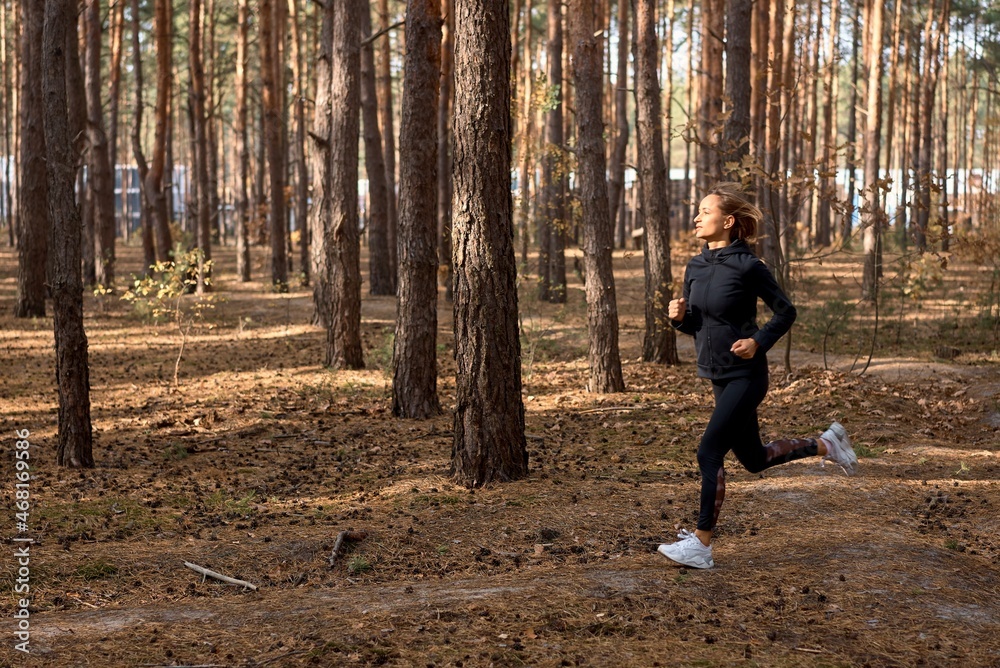 Young athletic woman jogging in forest in sunny morning. Healthy lifestyle concept. Young athletic woman jogging in forest in sunny morning. Healthy lifestyle concept.