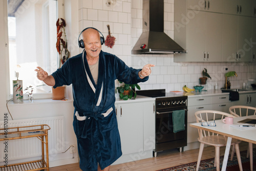 Cheerful senior man wearing headphones dancing in kitchen at home