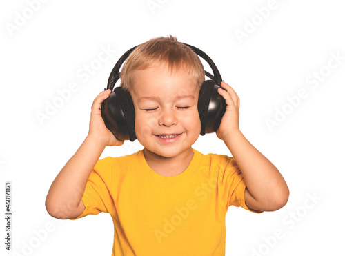 A cheerful, handsome little boy in a yellow T-shirt enjoys music. He presses the headphones to his head and ears. Isolate on a white background. Isolate on a white background