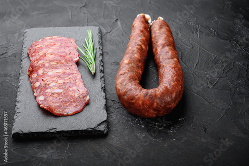 Whole and sliced chorizo sausage on black background