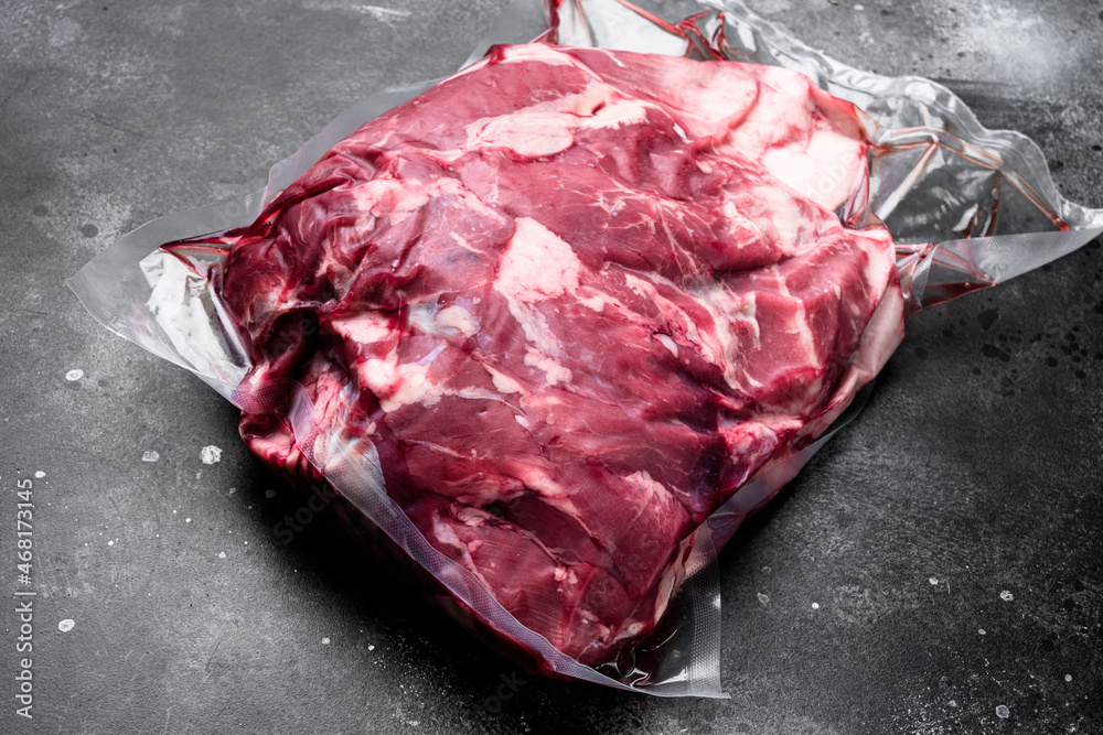 Fresh, raw, vacuum packed cut lamb meat, on black dark stone table background, with copy space for text