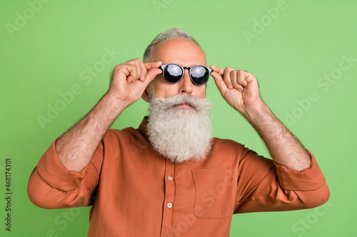 Portrait of attractive content serious grey-haired man touching specs weekend isolated over green color background © deagreez