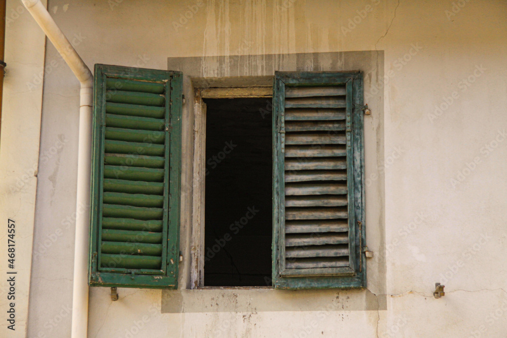 Green shutters on the window against a yellow colored wall. Old exterior in italian mediterranian village with closed Wooden vintage window with green blinds. Green shutters on the window against a yellow colored wall. Old exterior in italian mediterranian village with closed Wooden vintage window with green blinds.