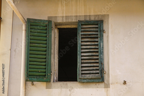 Green shutters on the window against a yellow colored wall. Old exterior in italian mediterranian village with closed Wooden vintage window with green blinds.