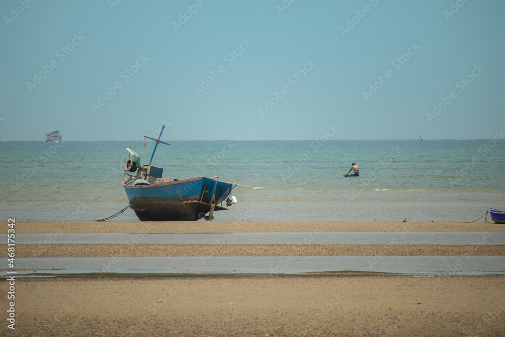 fisherman's fishing boat on sand at a fishing village beach There is an island and sea background with the daytime sky.  stranded fishing boat After the sea has receded