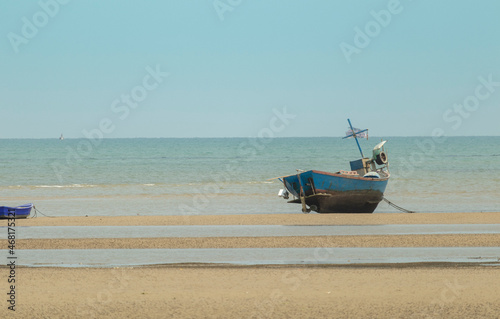 Fototapeta Naklejka Na Ścianę i Meble -  fisherman's fishing boat on sand at a fishing village beach There is an island and sea background with the daytime sky.  stranded fishing boat After the sea has receded