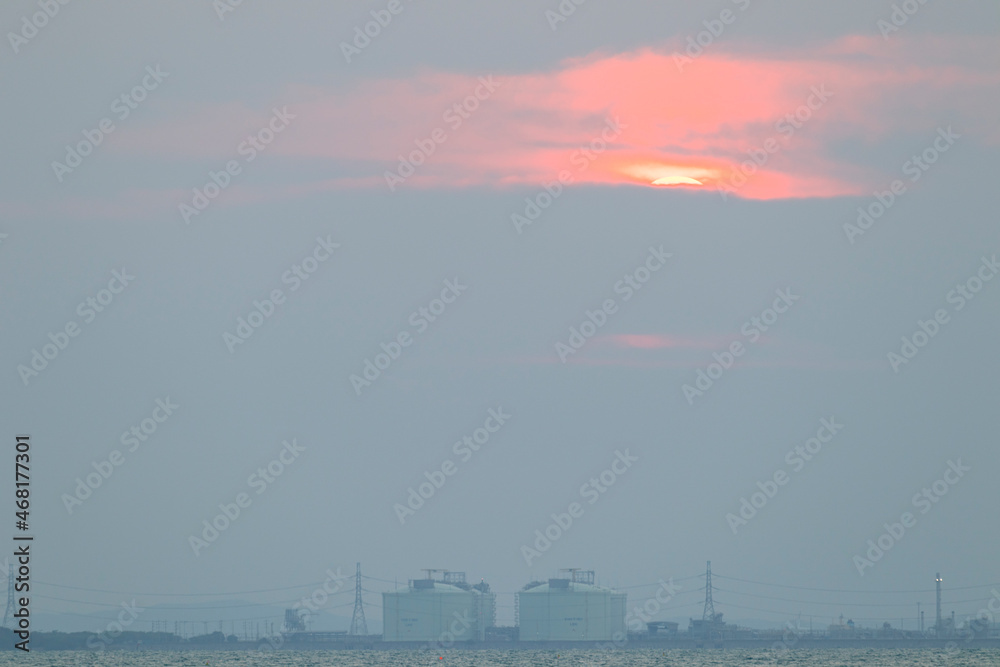  red sun in the sky and evening clouds are over Tangyard. In the petrochemical industry .The front is sea and white waves.