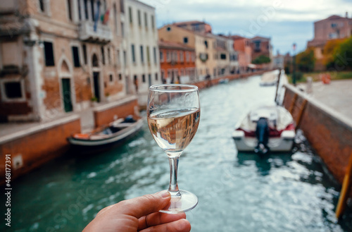 White wine glass for tasting during walking in Venice. Water canals and embankments with bar and restaurants of famous italian city