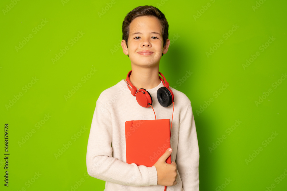Child boy in headphones holding book isolated over green background.
