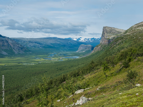 View on meandering glacial Rapadalen river delta valley at Sarek national park, Sweden Lapland with Skierffe rock peak, snow capped mountains and birch trees. Summer day, white clouds photo