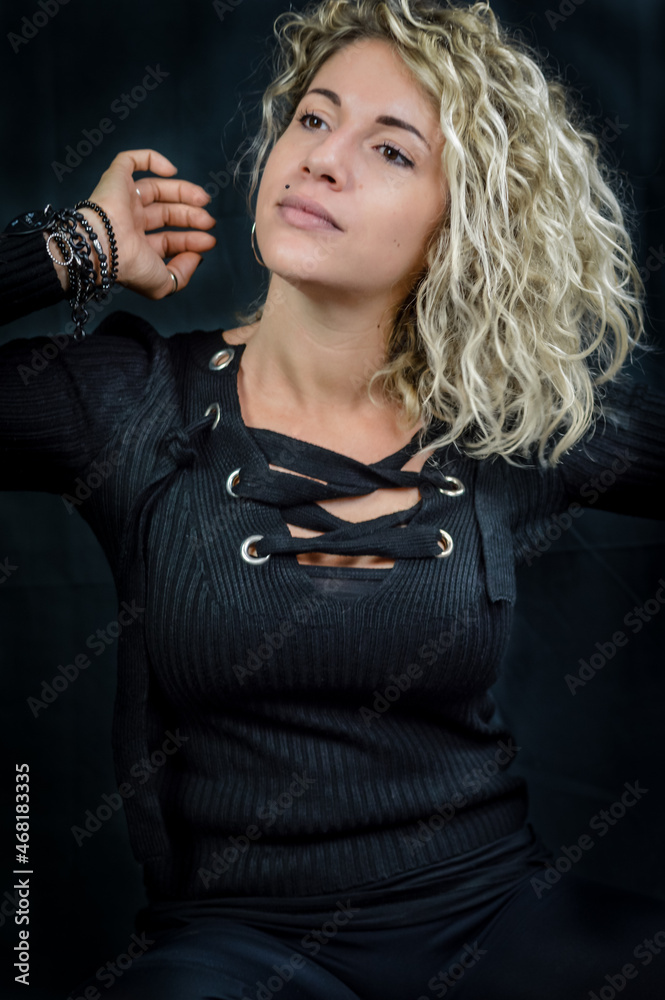 Portrait of a beautiful young woman with blond curly hair adjusting her hair and looking away Portrait of a beautiful young woman with blond curly hair adjusting her hair and looking away