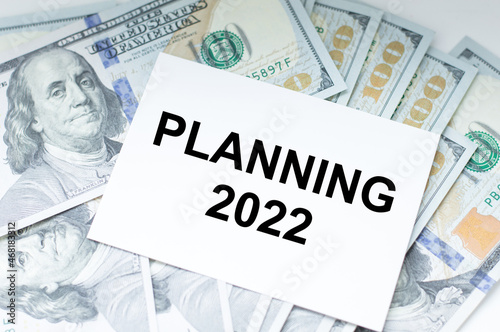 Text PLANNING 2022 on a white card against the background of money dollars on the table, business concept, plans for the new year