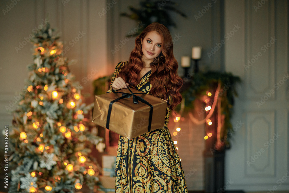 A young beautiful woman in an elegant dress with a gift near the Christmas tree
