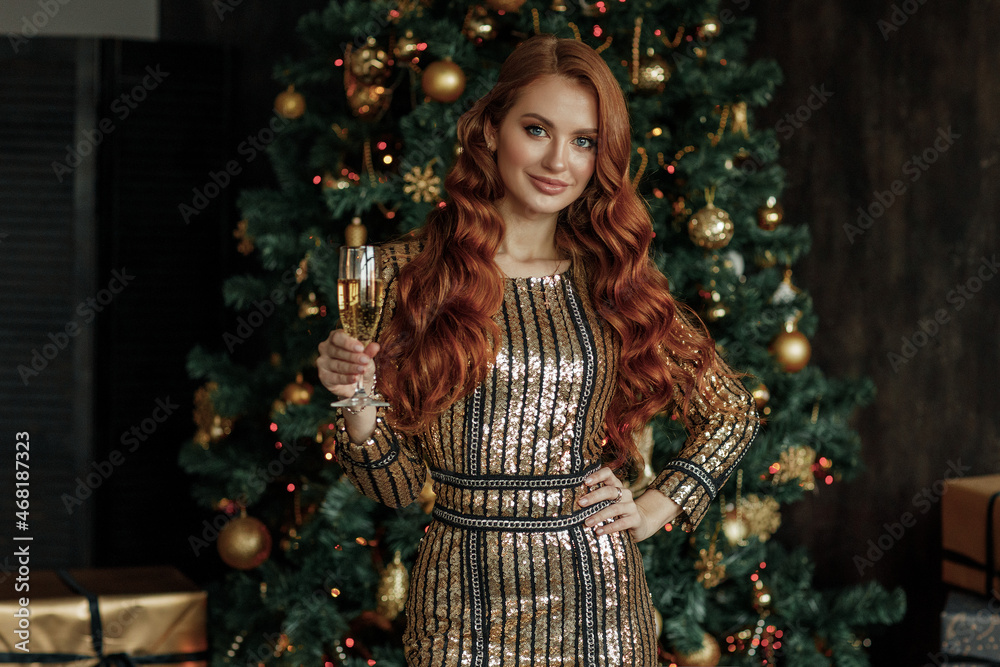 A young beautiful woman with a glass of champagne near the Christmas tree
