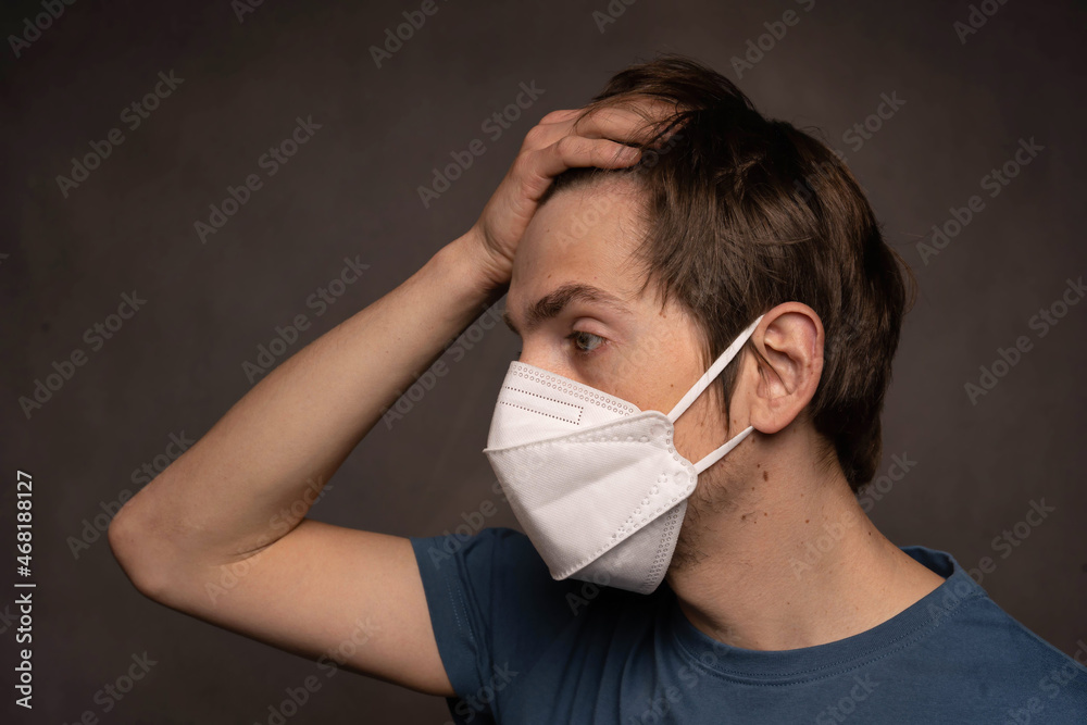 Young handsome tall slim white man with brown hair concerned wearing face mask in blue shirt on grey background Young handsome tall slim white man with brown hair concerned wearing face mask in blue shirt on grey background