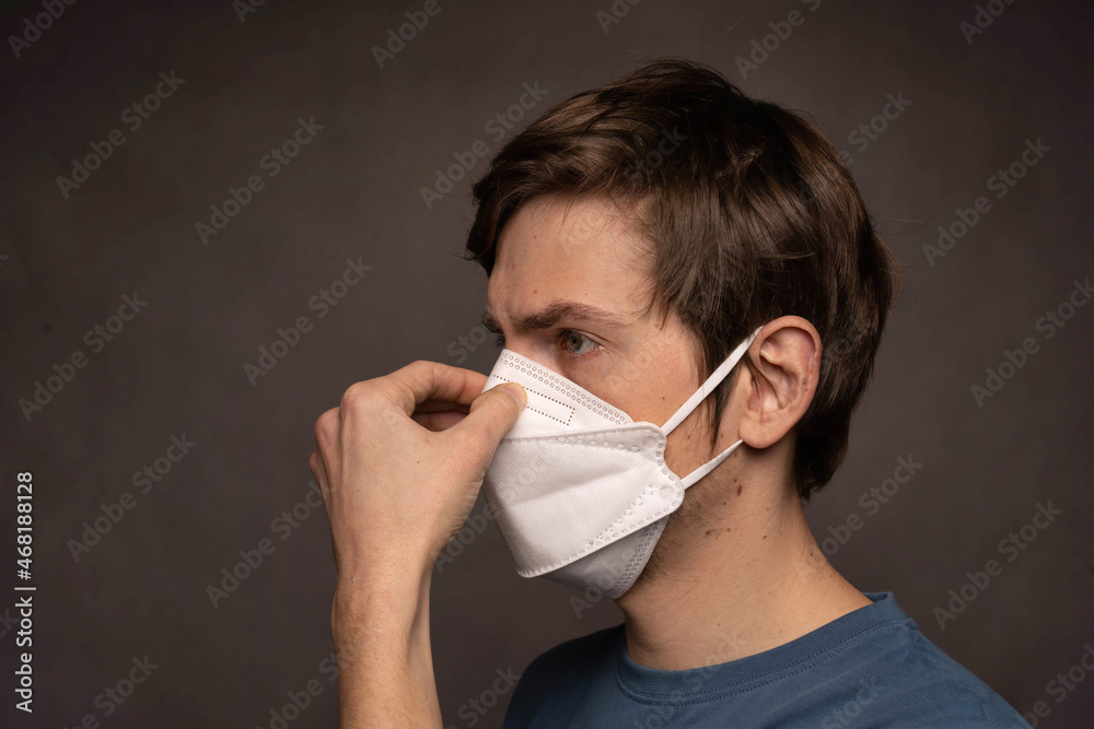 Young handsome tall slim white man with brown hair holding his nose wearing face in blue shirt on grey background