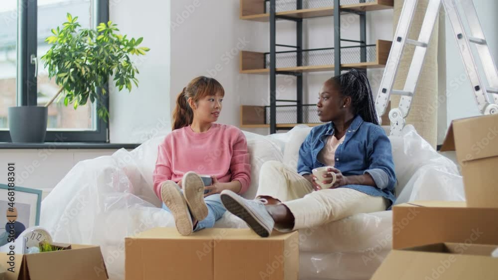 people, repair and real estate concept - smiling women with stuff moving to new home, drinking coffee or tea and talking people, repair and real estate concept - smiling women with stuff moving to new home, drinking coffee or tea and talking
