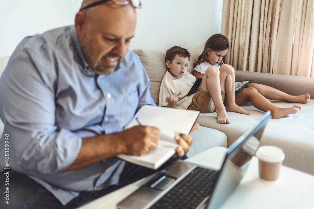 Obraz premium Cropped shot of a working father multitasking. Single father with a kids trying to work from home. Young father stay at home trying to work on laptop while his children sit beside him.