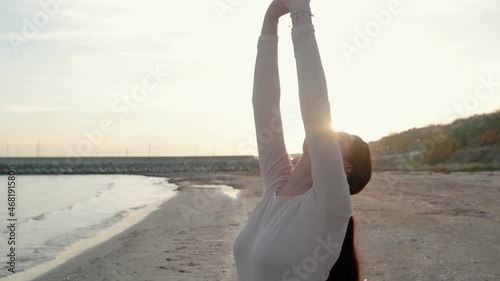 Athletic woman doing aerobics, body flexibility, warm up workout outdoors in slow motion seascape, raises arms