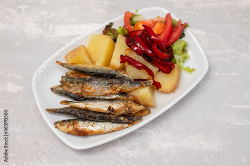 fried sardines with boiled potato and salad on white dish