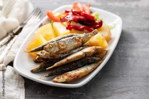 fried sardines with boiled potato and salad on white dish
