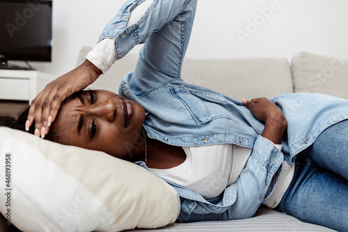 Woman lying on sofa looking sick in the living room. Beautiful young woman lying on bed and holding hands on her stomach. Woman having painful stomach ache on bed, Menstrual period. photo