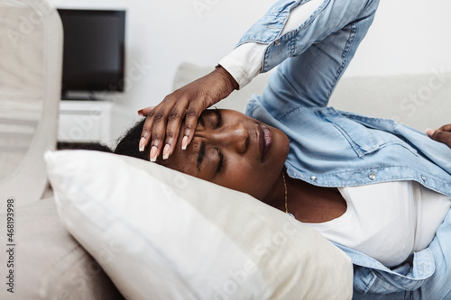Woman in painful expression holding hands against belly suffering menstrual period pain, lying sad on home bed, having tummy cramp in female health concept.