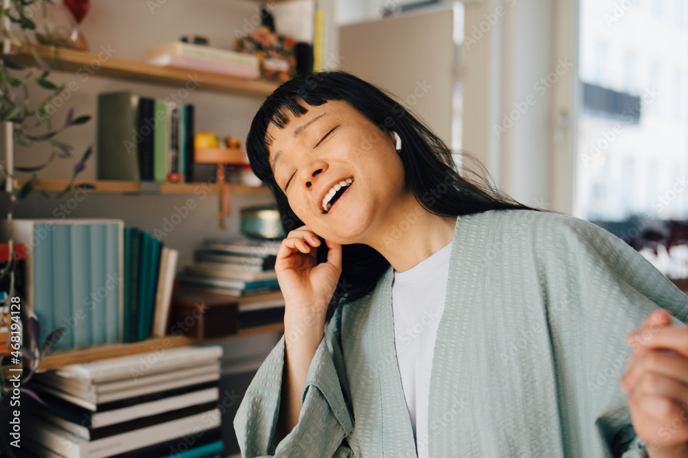 © Maskot - Young woman listening music through wireless in-ear headphones at home