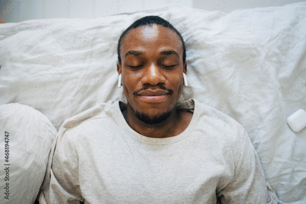 Smiling man wearing wireless in-ear headphones while relaxing with eyes closed Smiling man wearing wireless in-ear headphones while relaxing with eyes closed