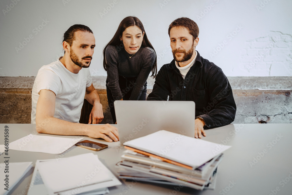 Male and female professionals working over laptop on table in startup company Male and female professionals working over laptop on table in startup company