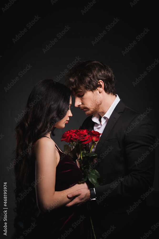 side view of brunette woman with red roses standing face to face with man on dark background side view of brunette woman with red roses standing face to face with man on dark background
