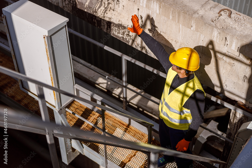 Matured man factory worker wearing safety helmet and work vest while working at manufacturing plant