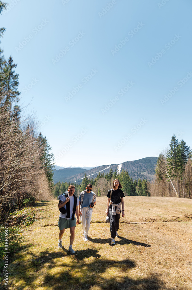 Three friends in stylish casual clothes on vacation walk together in the mountains against the backdrop of a beautiful landscape. Active rest of tourists in the mountains.